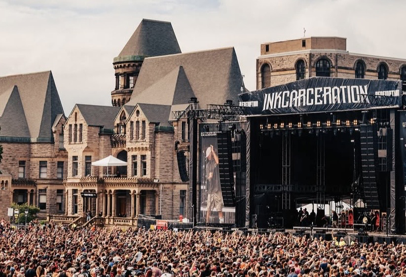 Editorial illustration of rock fans in practical festival clothing watching an outdoor stage beside a historic stone reformatory.